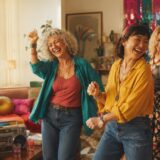 明るい部屋で音楽に合わせて踊り笑う40代から60代の女性たち