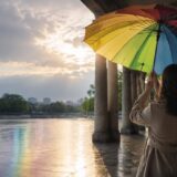 雨上がりの光の中でカラフルな傘を開く女性の後ろ姿