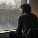 雨の窓辺で後悔を抱えて座る男性を描いたJealous Guy英語学習記事のイメージ