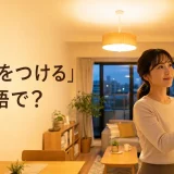 夕方のリビングで女性が壁のスイッチを押して電気をつける様子。「電気をつける」は英語で?